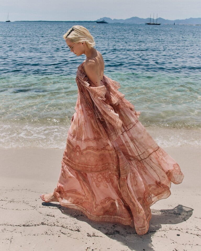 Pom Klementieff: Walks along the shore in a long, flowing dress in pink tones that…