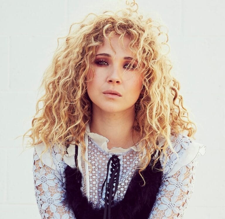 Juno Temple: Luce una blusa de encaje blanco con detalles en negro y un corte romántico,…