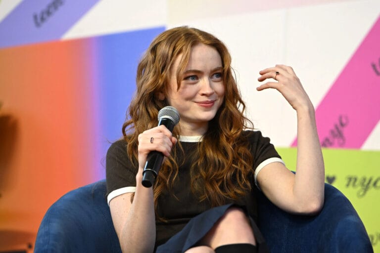 Sadie Sink: Wears a short-sleeved blouse in dark tones with details at the collar,…