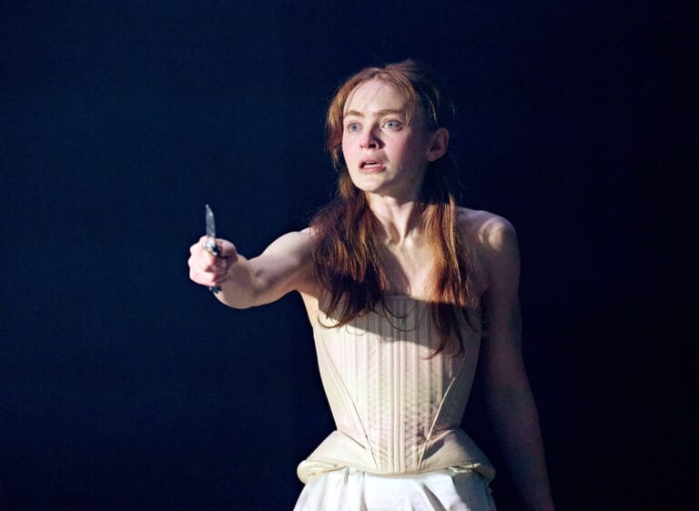 Sadie Sink: Wears a light, fitted corset with a skirt that flows downward, while…