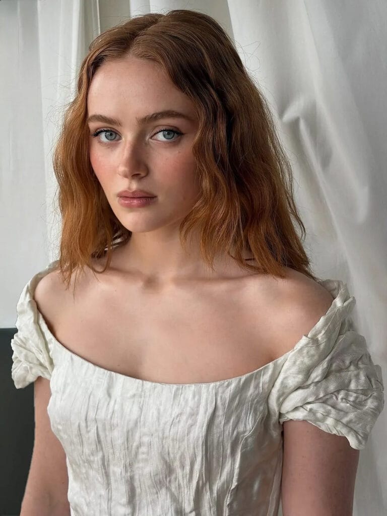 Sadie Sink: Wearing a white dress with a full cut and puffed sleeves that highlights her…