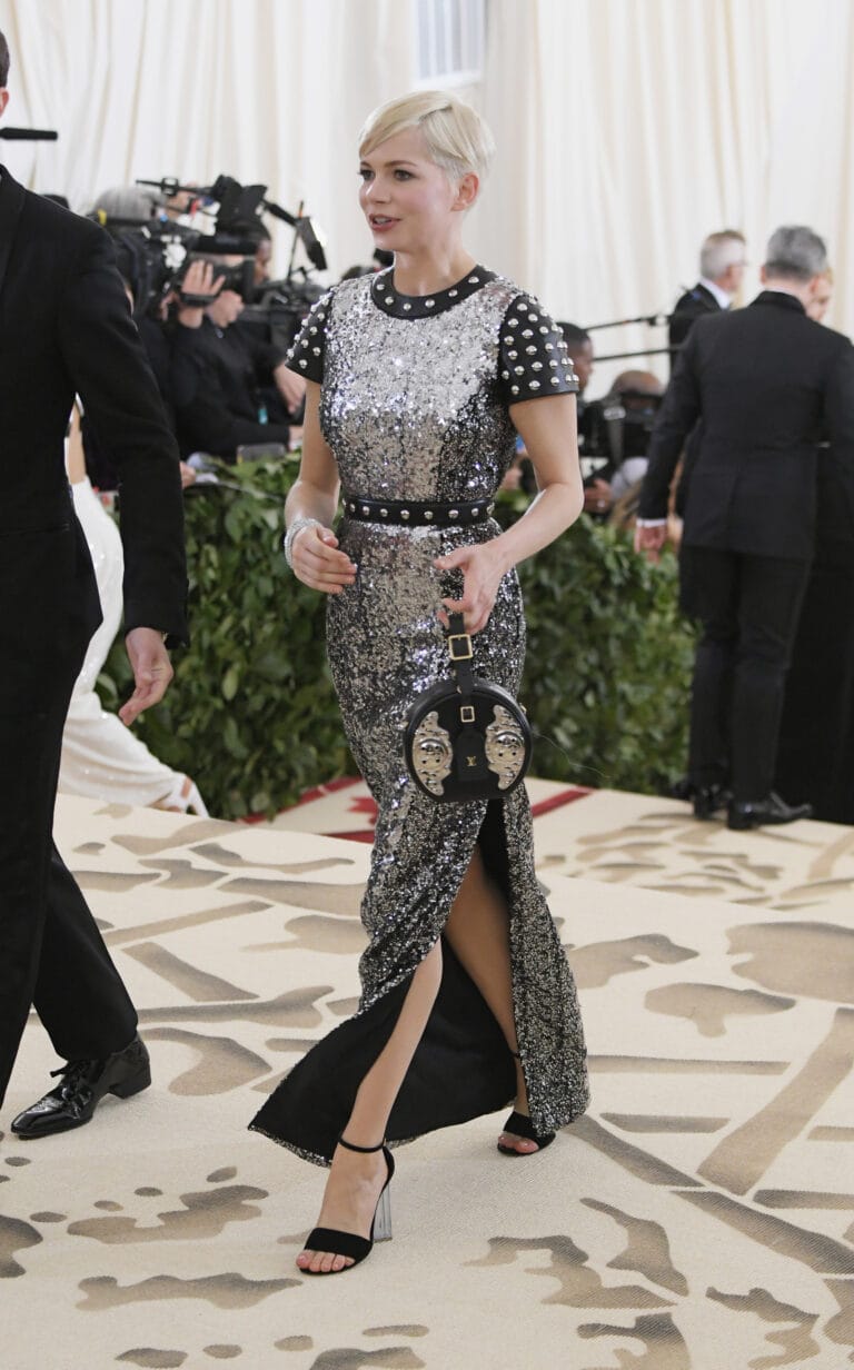 Michelle Williams: Wears a long, fitted silver sequin gown with black details, which…