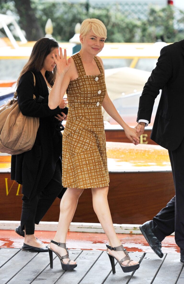 Michelle Williams: She wears a brown dress with a plaid pattern and buttons on the front…