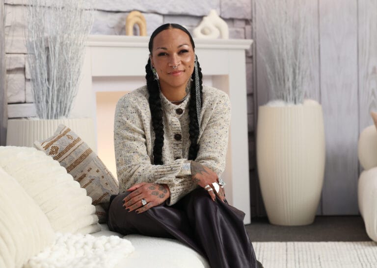 Kali Reis: Wears a light-toned knit sweater with buttons while sitting on…