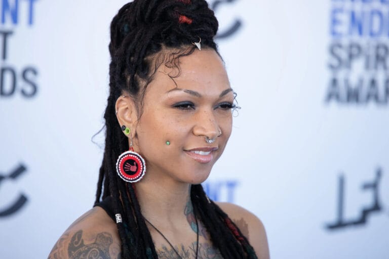 Kali Reis: Wearing a black sleeveless top that showcases her tattoos, while wearing earrings of…