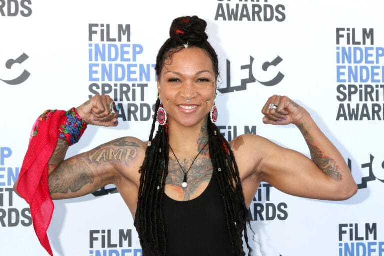 Kali Reis: Wearing a fitted black top that highlights her figure, while flexing her muscles with…
