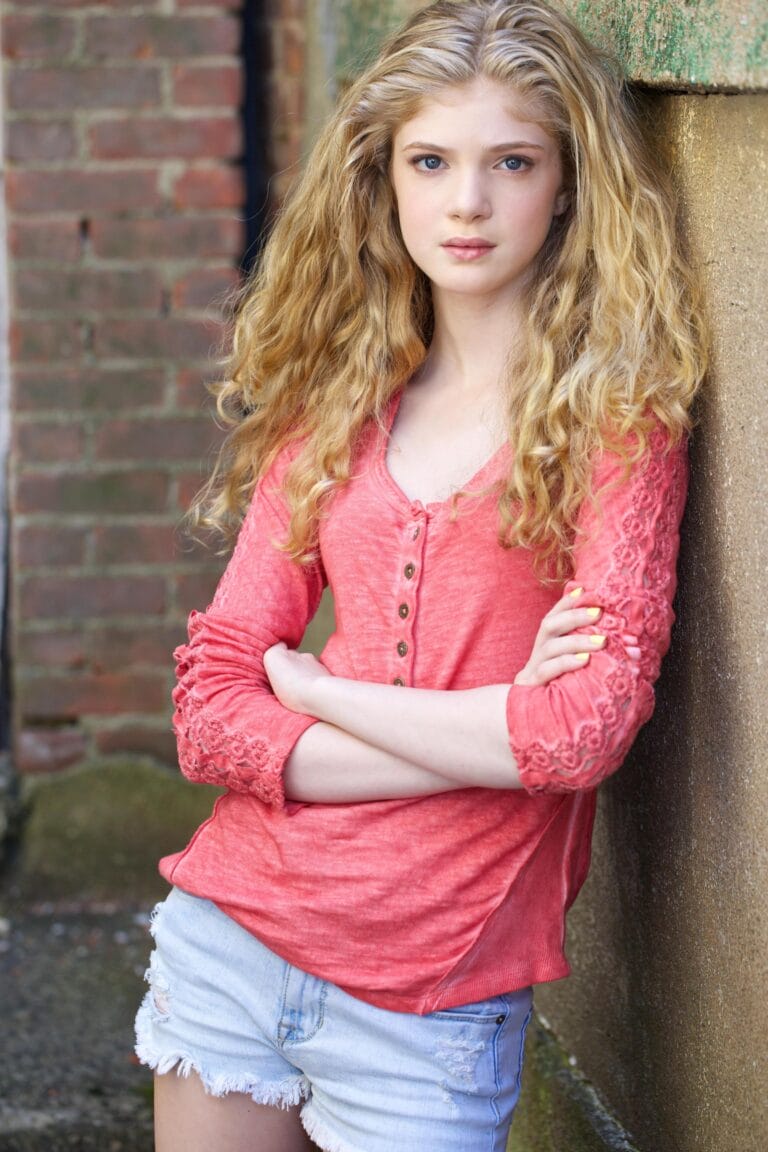 Elena Kampouris: Wearing a long-sleeve coral blouse with lace details on…