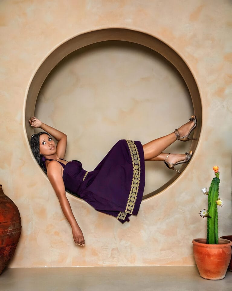 Toks Olagundoye: Poses casually inside a large circle, wearing a purple dress with…