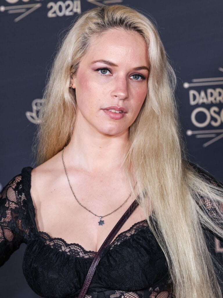 Alexis Knapp: Luce un top de encaje negro que resalta su figura, complementado con un collar…