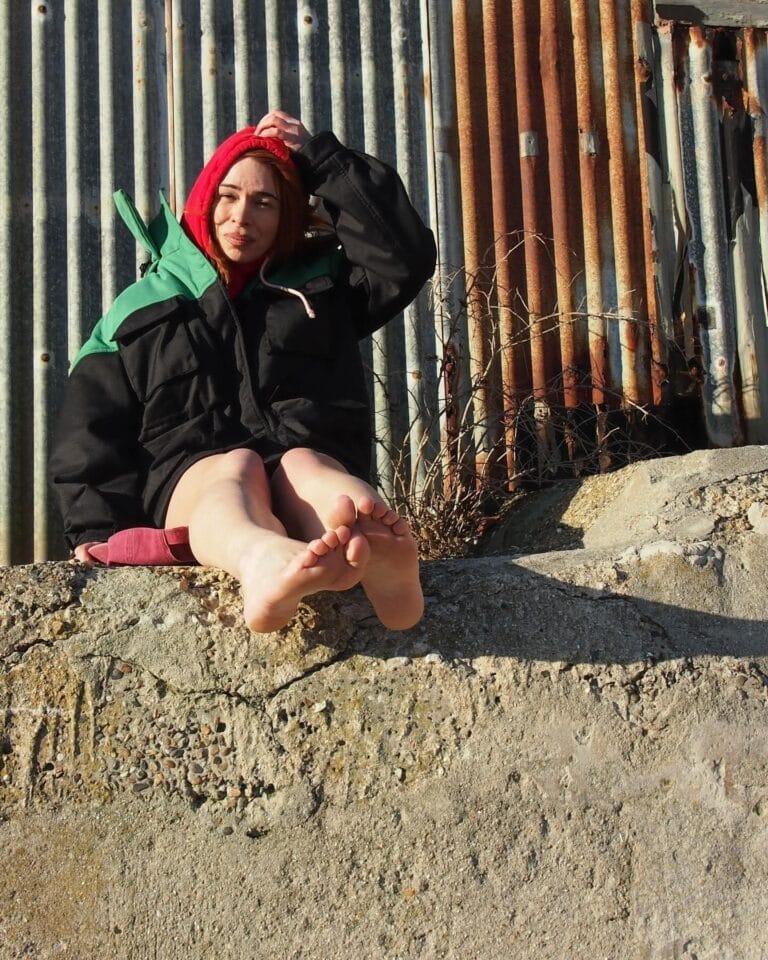 Billie Piper: Wears an oversized black jacket with green details and a red sweatshirt underneath,…