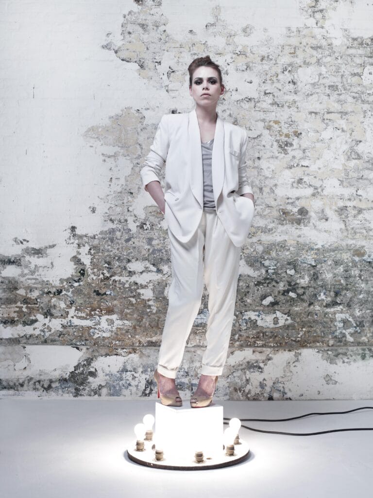 Billie Piper: Stands on an illuminated platform, dressed in a white suit that matches…