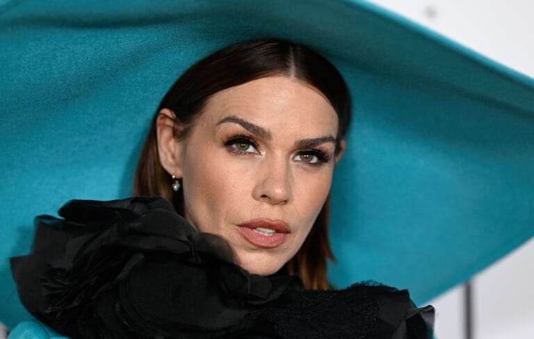 Billie Piper: Wears a striking blue hat that frames her face, complemented by an elegant coat…