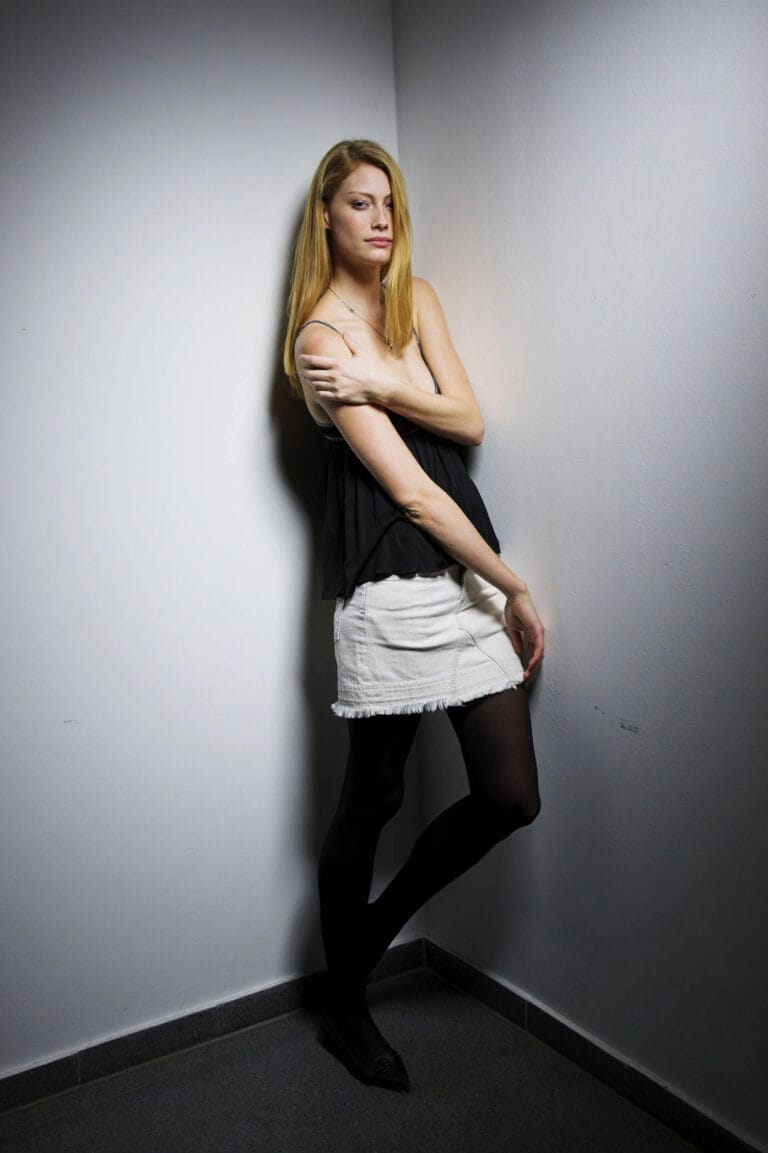 Alyssa Sutherland: Wears a loose, lightweight black sleeveless blouse paired with a white mini skirt…