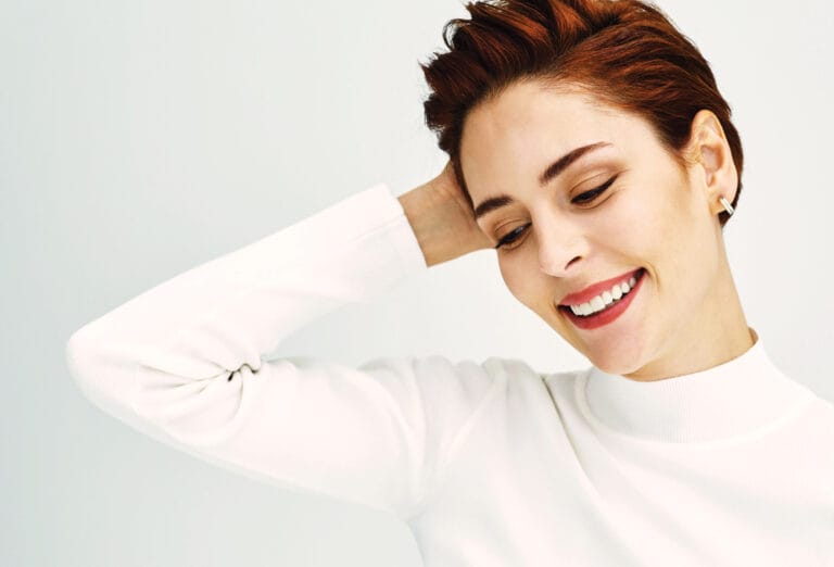 Yıldız Çağrı Atiksoy: Wears a white turtleneck sweater, smiling brightly as she runs her hand through…