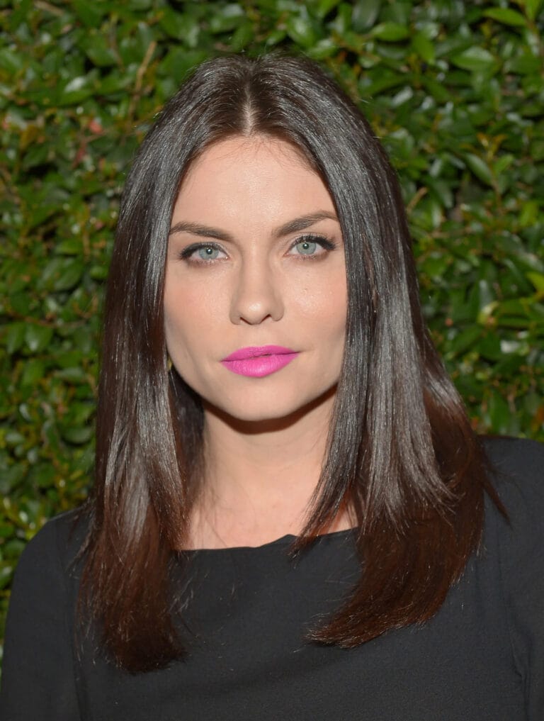 Jodi Lyn O’Keefe: Wears a simply cut black blouse, highlighting her elegance with makeup that…