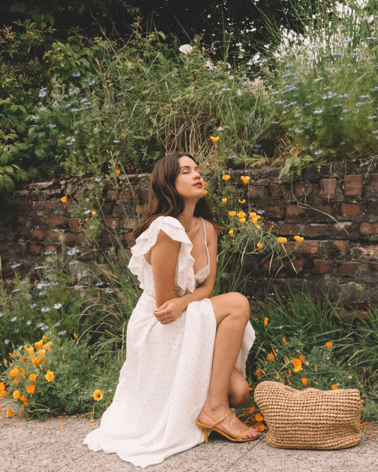 Sarah Butler: Wears a white dress with delicate ruffles, sitting on a stone surface with…