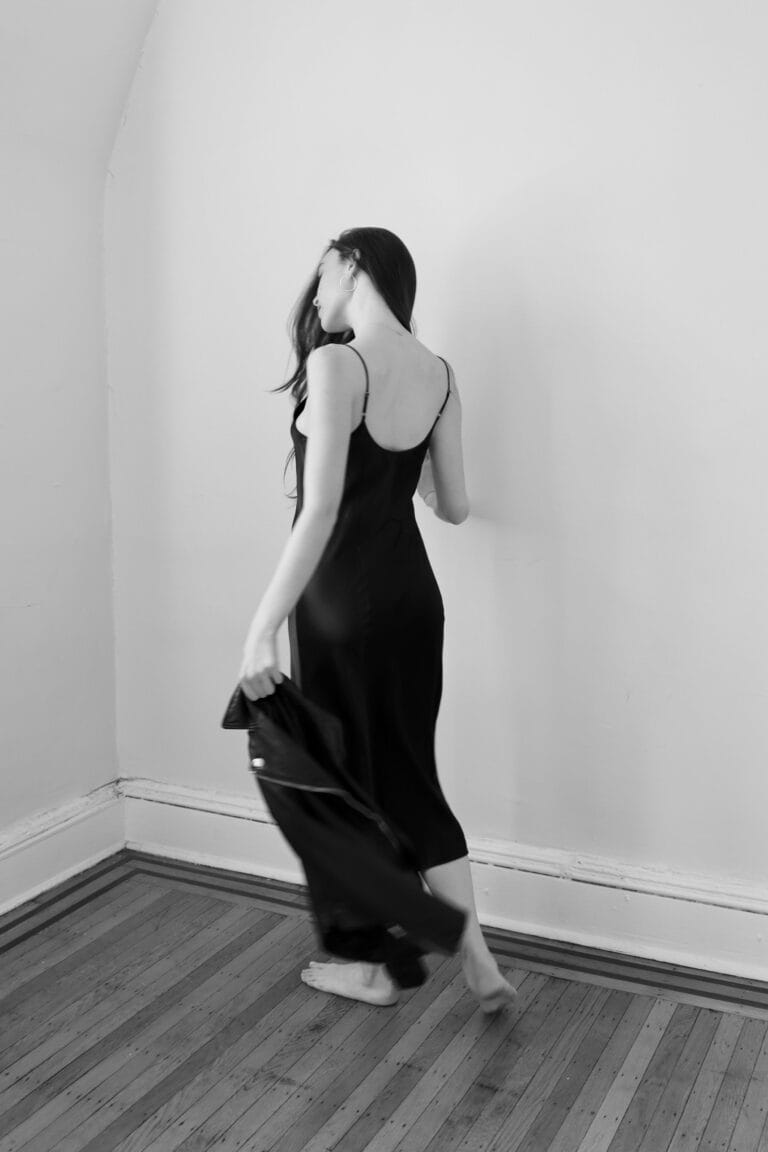 Ella Beatty: Wears a black dress with thin straps, elegant and flowing, while walking away with…