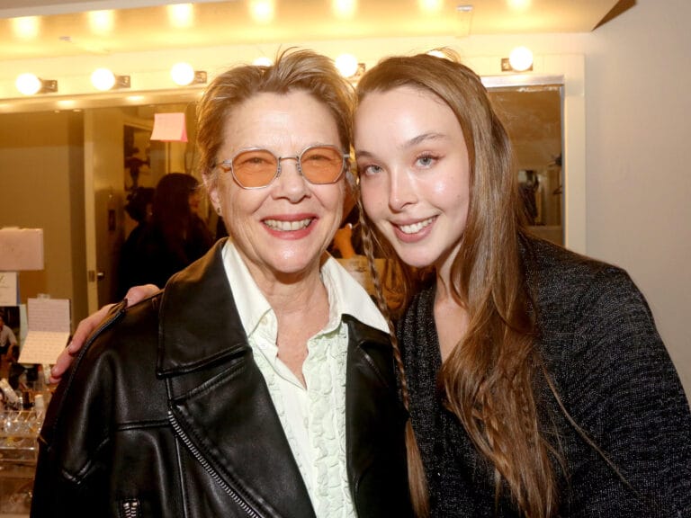 Ella Beatty: Wears a black leather jacket over a white blouse and smiles confidently,…