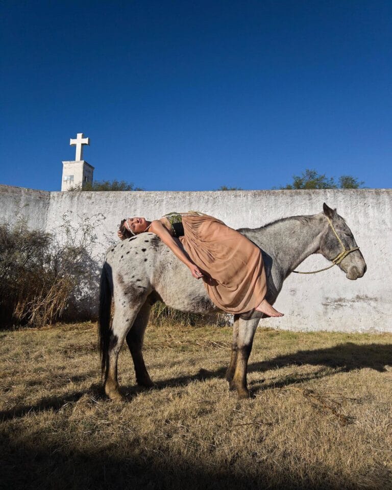 Vicky Krieps: Lies on a gray horse, wearing a long nude-toned dress that…