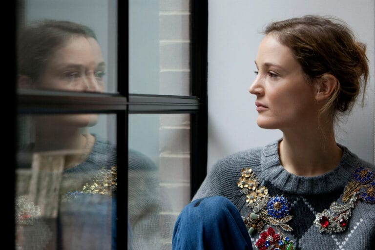 Vicky Krieps: Poses in a gray sweater decorated with colorful brooches, leaning on the…