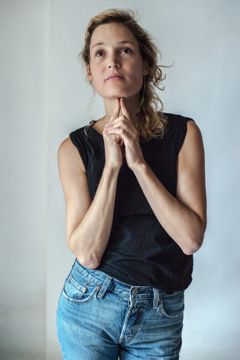 Vicky Krieps: Wears a black sleeveless tee and high-waisted skinny jeans, with a…