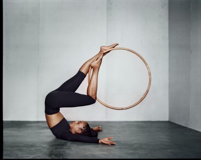 Kerry Washington: Wears a black leggings and top set, striking an impressive acrobatic pose, resting…