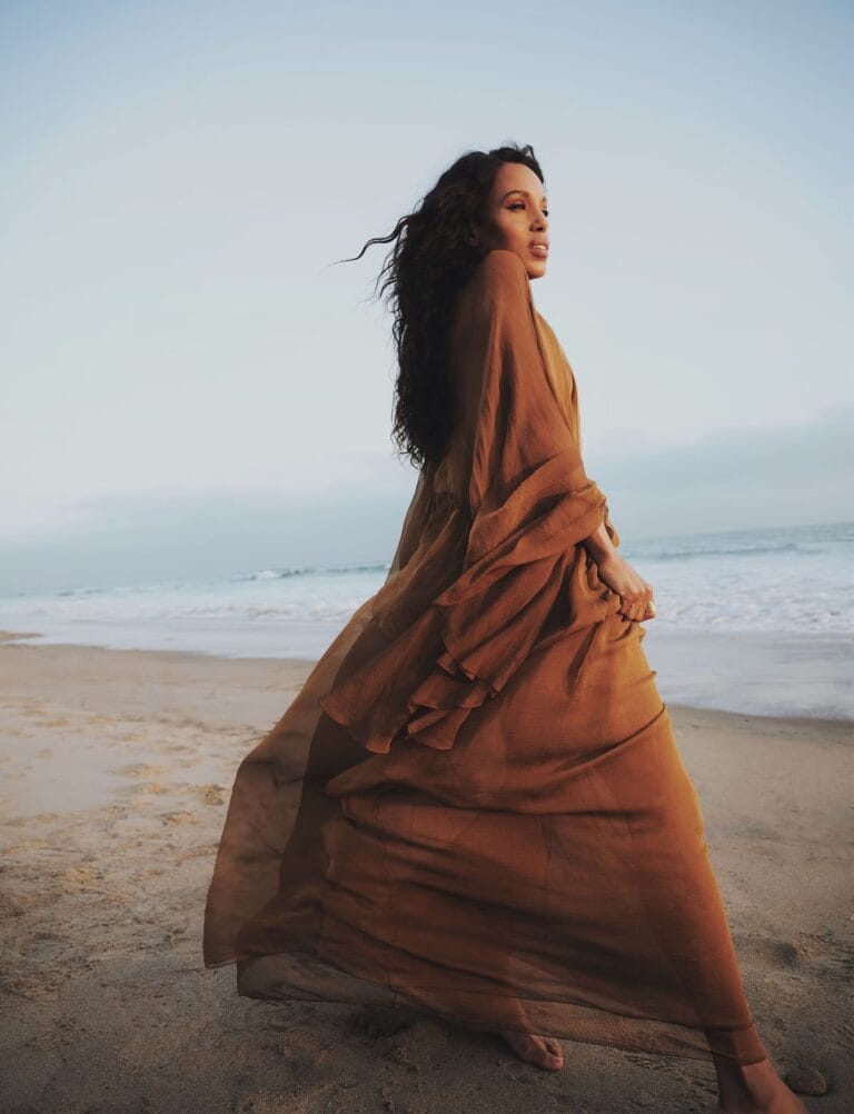 Kerry Washington: Wears a long, flowing terracotta dress with wide sleeves that…
