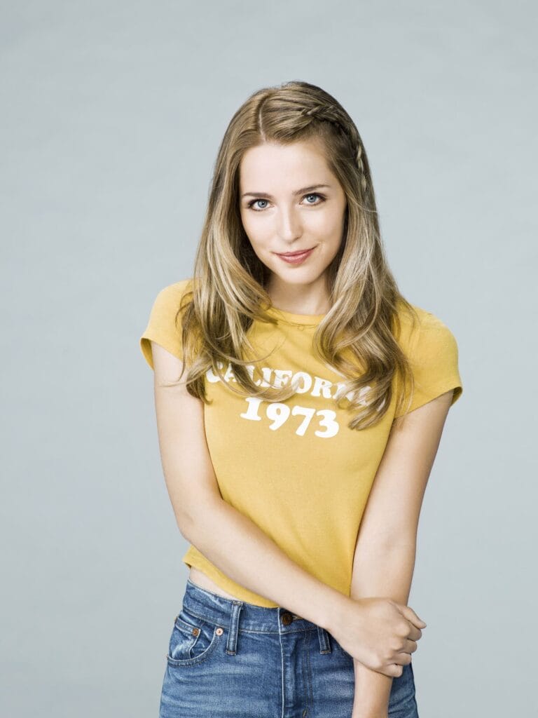 Jessica Rothe: Wears a yellow T-shirt with the text "California 1973" and fitted denim jeans.…