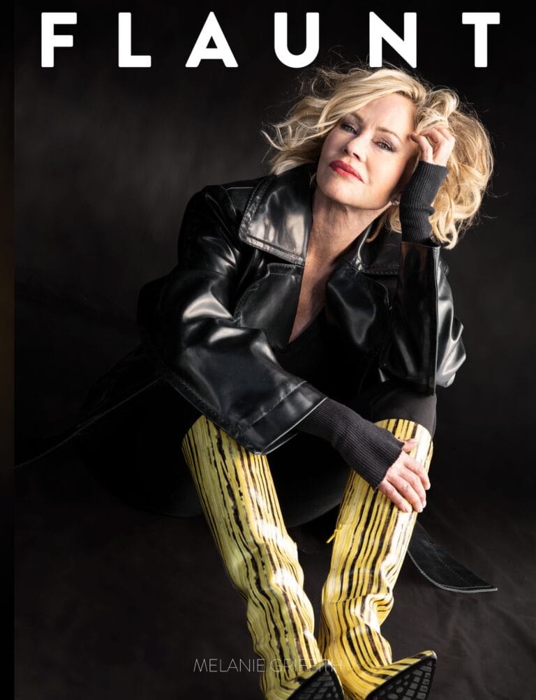 Melanie Griffith: Wears an oversized black leather jacket and long yellow striped boots, seated…