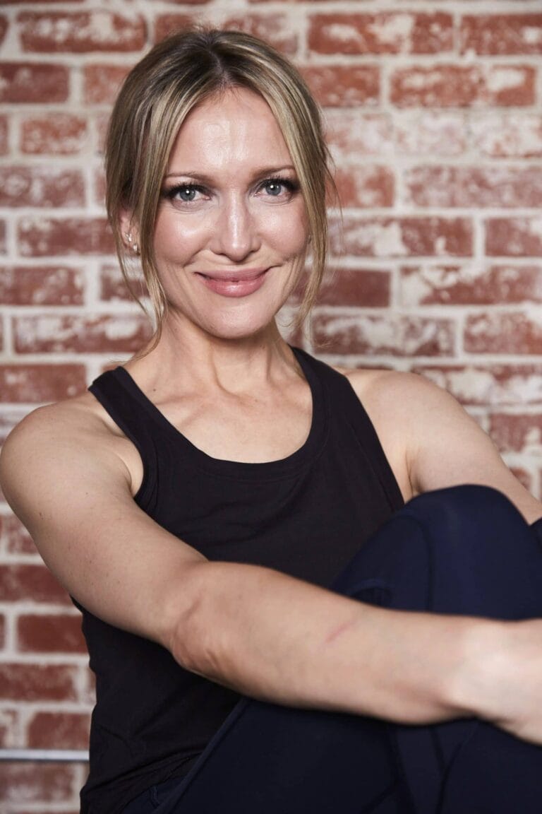 Kate Beahan: Wearing a relaxed, comfortable black tank top, leaning against the…