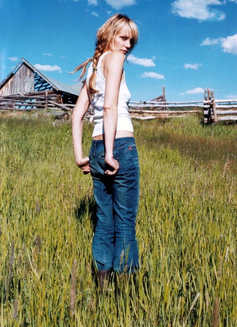 Daryl Hannah: Poses in a green field, wearing a sleeveless white top and fitted jeans.…