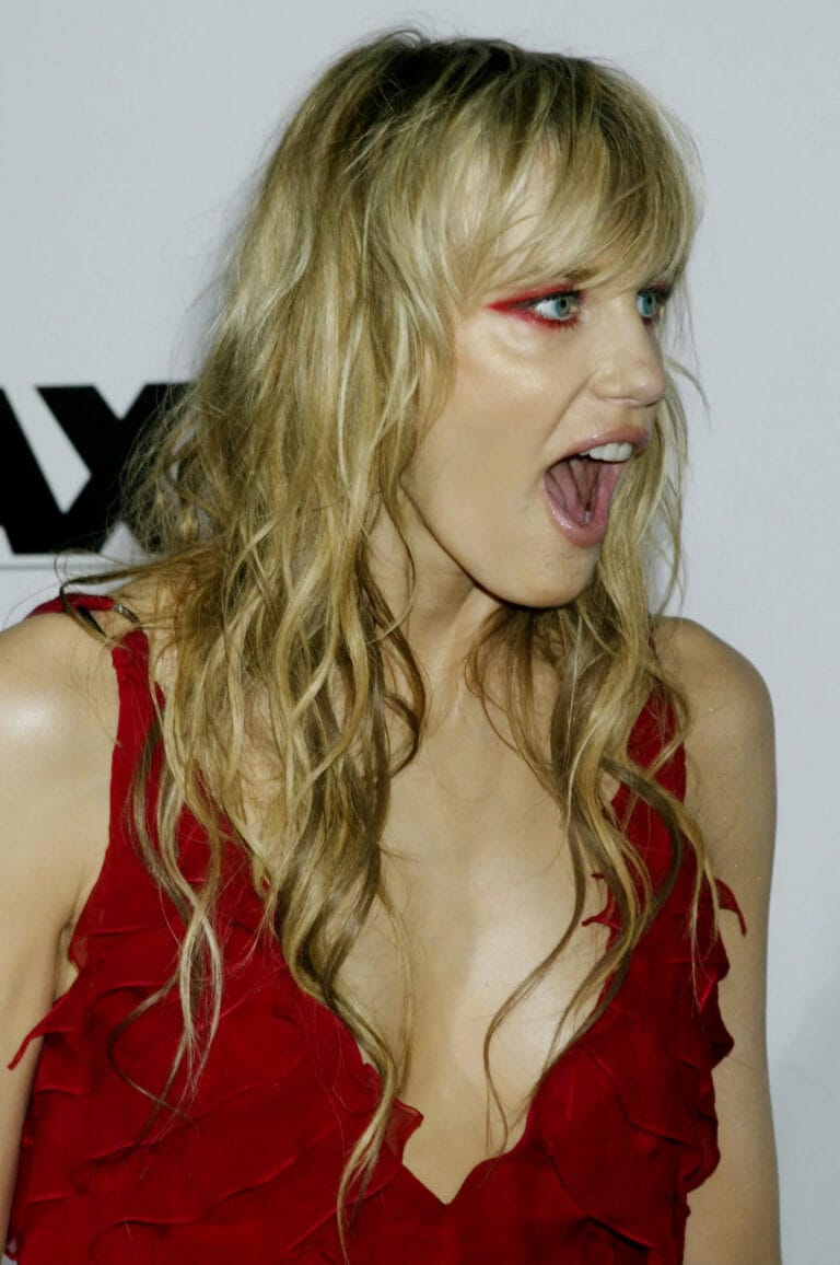 Daryl Hannah: Wears a red dress with ruffles and a deep neckline while expressing surprise or…