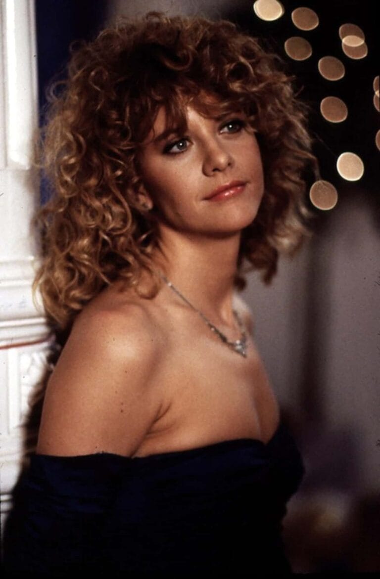 Meg Ryan: Wears an elegant dark blue bardot-neckline dress that highlights her shoulders as she…