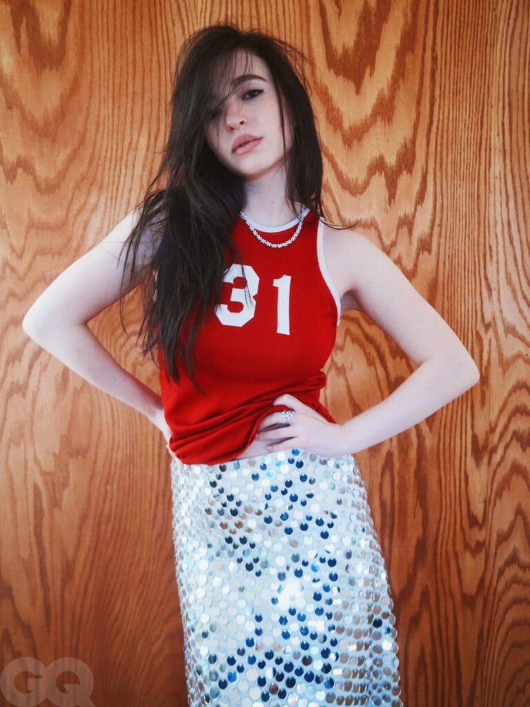 Mikey Madison: Wears a red sleeveless top with the number 31, paired with a skirt…