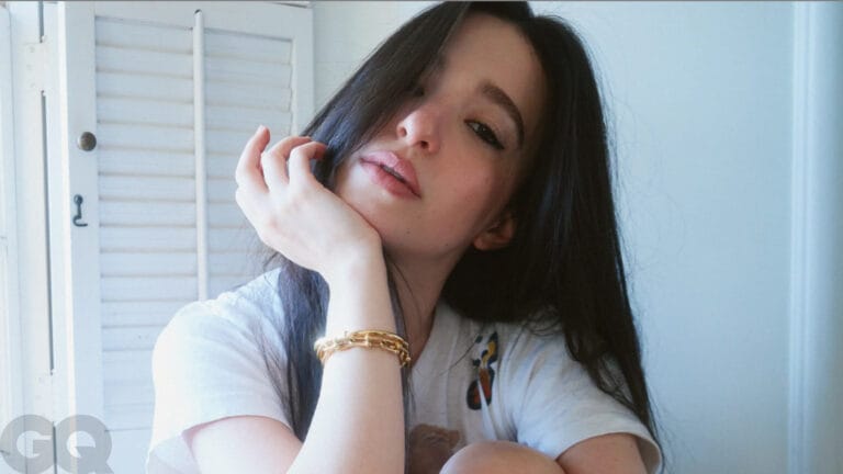 Mikey Madison: Wears a white T-shirt with a simple design, resting her head on one hand…