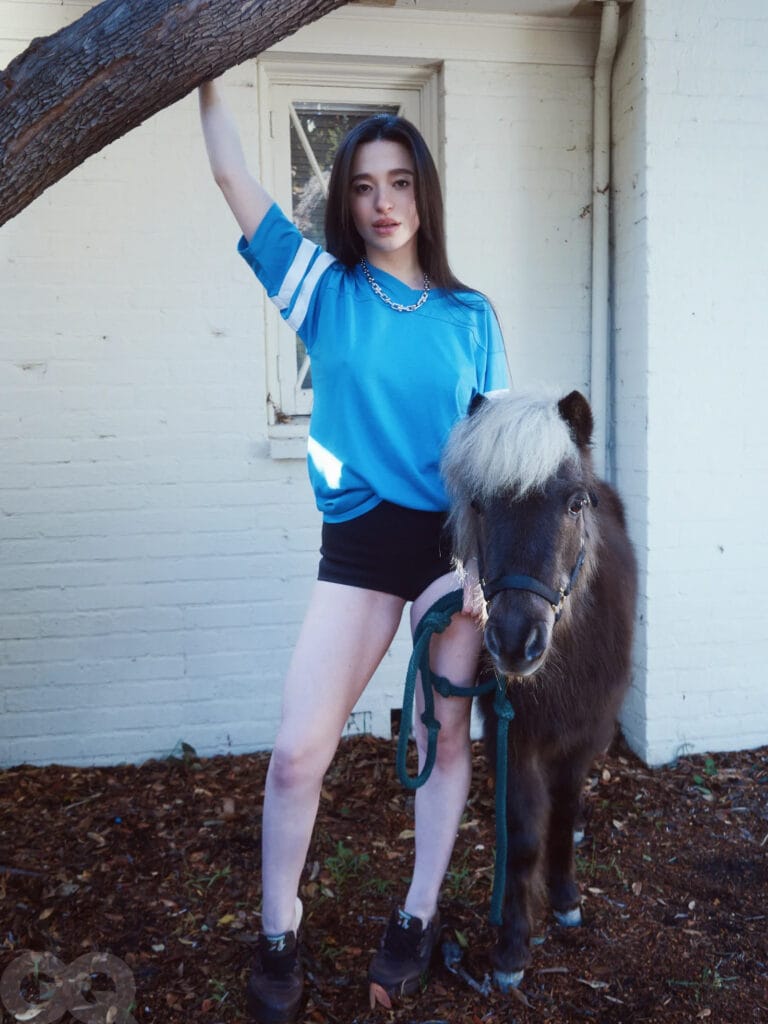Mikey Madison: Poses in a blue t-shirt with white details and black shorts, with a…