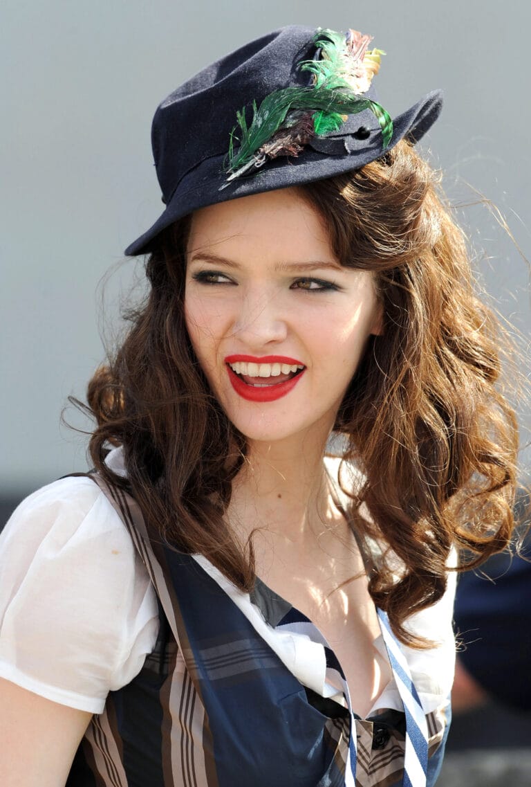 Talulah Riley: Luce un sombrero negro adornado con plumas, que resalta su sonrisa radiante y labios…