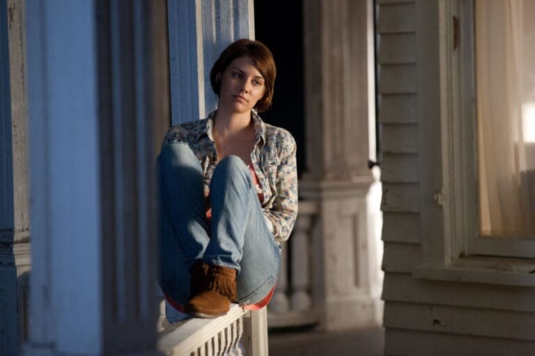 Lauren Cohan: Está sentada sobre el borde de un porche, con las piernas recogidas y apoyadas…