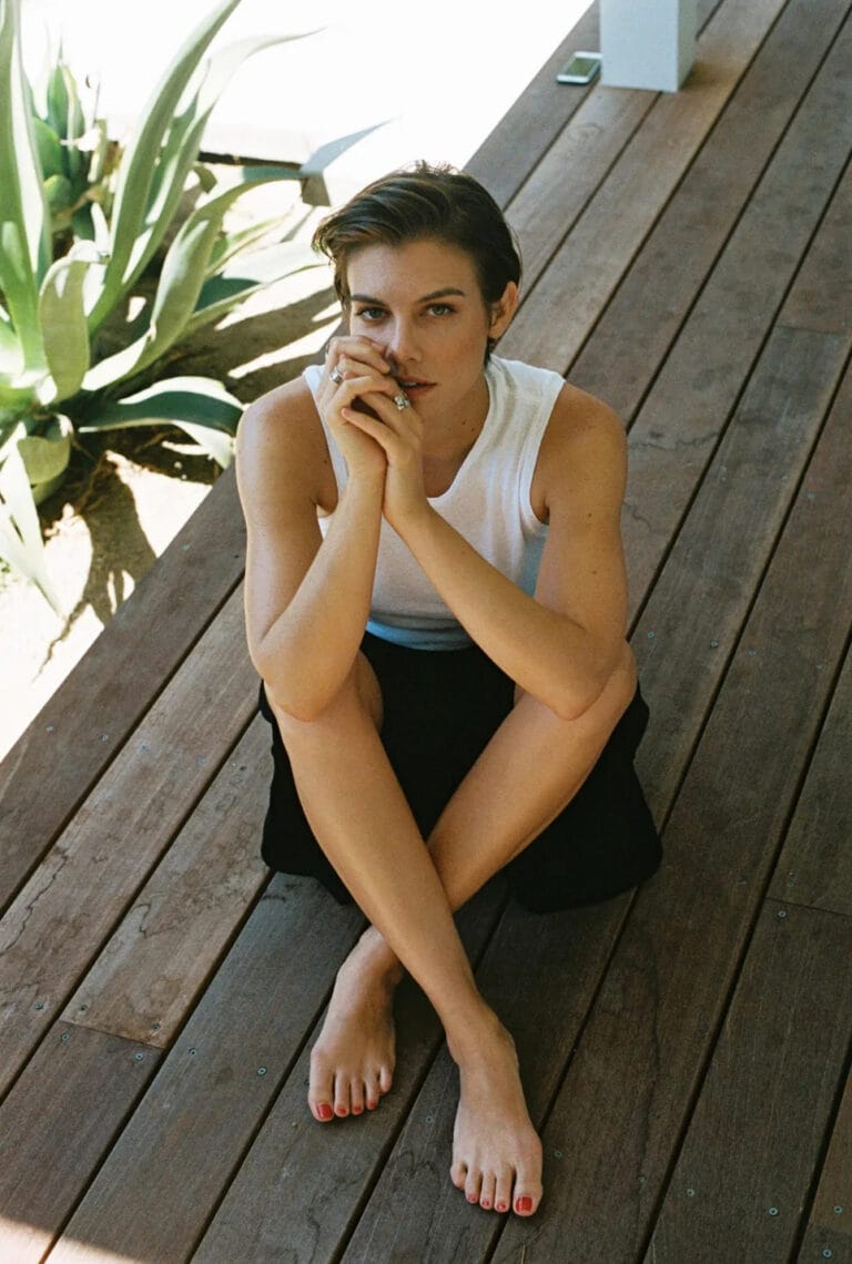 Lauren Cohan: Posa sentada sobre un suelo de madera, con las piernas cruzadas y los pies…
