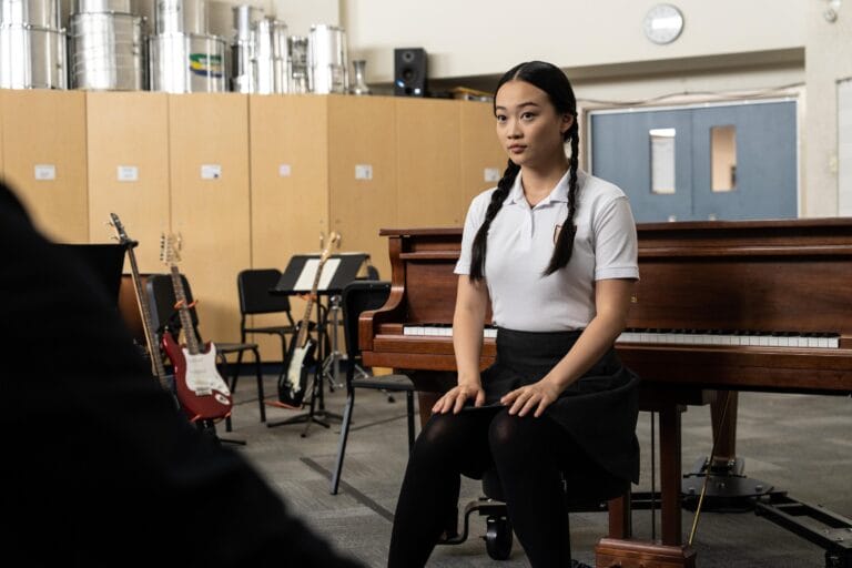 Callina Liang: Luce una camisa blanca y una falda corta negra, sentada en un piano con…