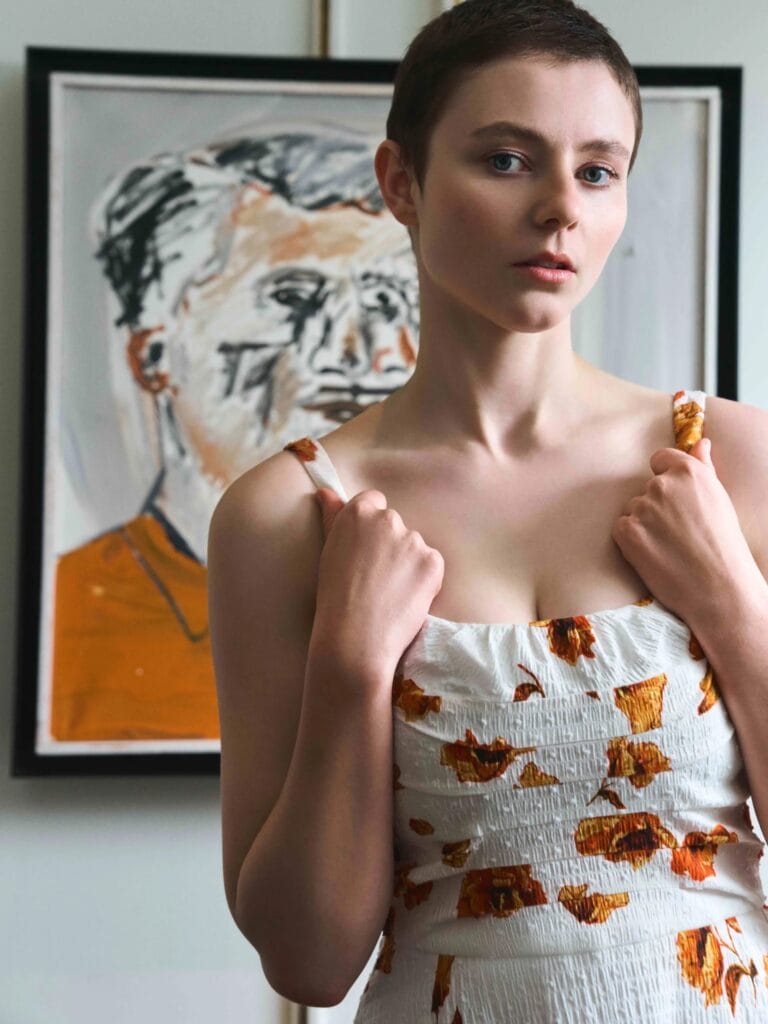Thomasin McKenzie: Luce un vestido blanco con estampado de flores naranjas, sosteniendo suavemente los tirantes con…