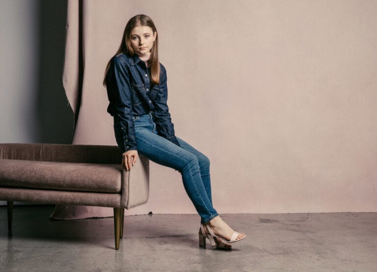 Thomasin McKenzie: Está sentada en un sofá de terciopelo, luciendo una camisa de mezclilla de manga…