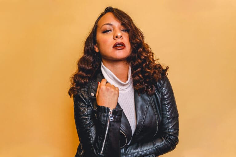 Jasmine Cephas Jones: Luce una chaqueta de cuero negra ajustada sobre un suéter de cuello alto blanco,…