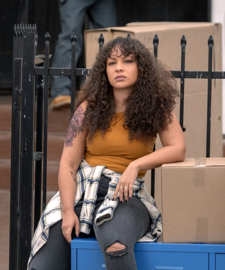 Jasmine Cephas Jones: Luce una camiseta sin mangas mostaza, sentada sobre una caja azul con una actitud…
