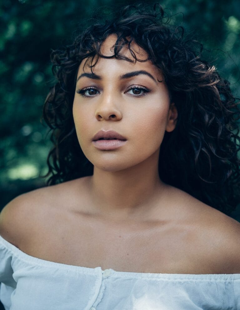 Jasmine Cephas Jones: Luce una blusa blanca de corte off-shoulder, que resalta su piel bronceada y suave.…