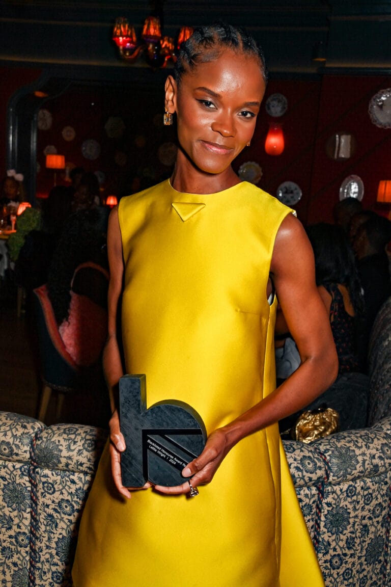 Letitia Wright: Luce un vestido amarillo vibrante, sin mangas y con un corte moderno, mientras sostiene…