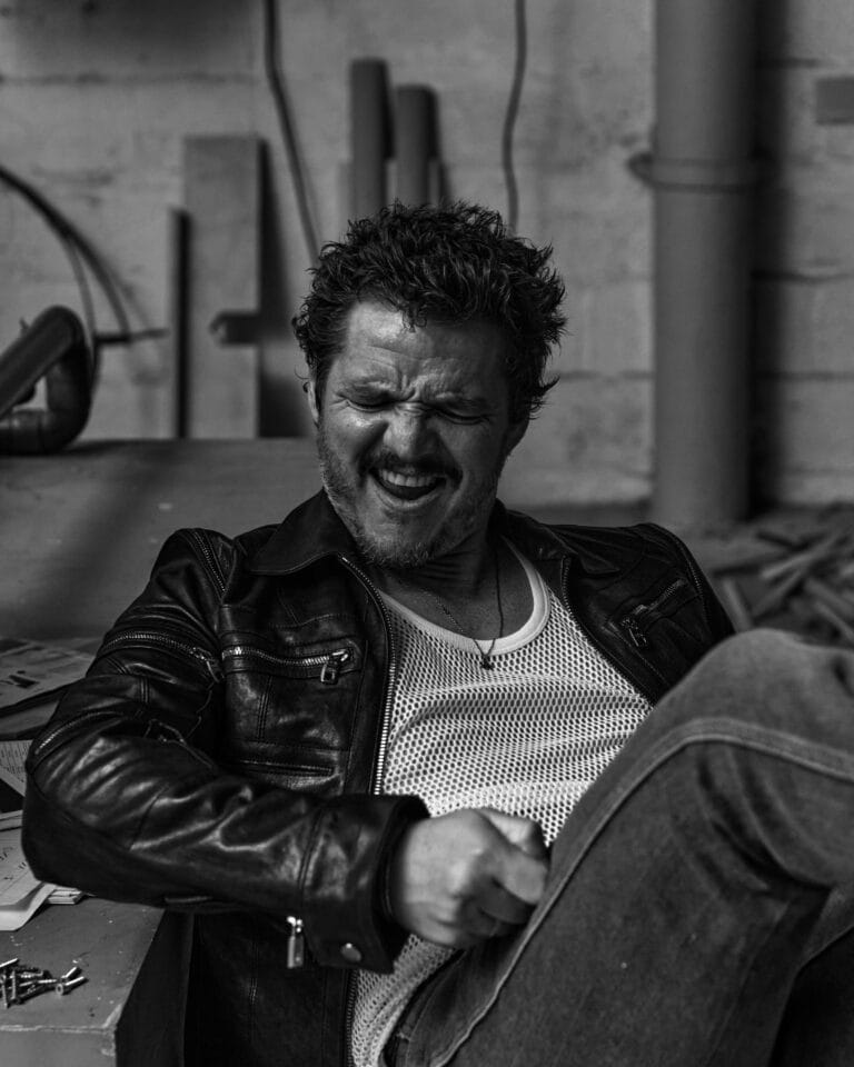 Pedro Pascal: Luce una chaqueta de cuero negro sobre una camiseta de malla blanca, sentado con…