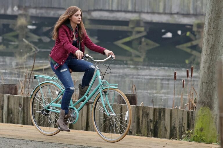 Chloë Grace Moretz: Riding a aqua-colored bicycle with confidence, wearing a burgundy coat over…